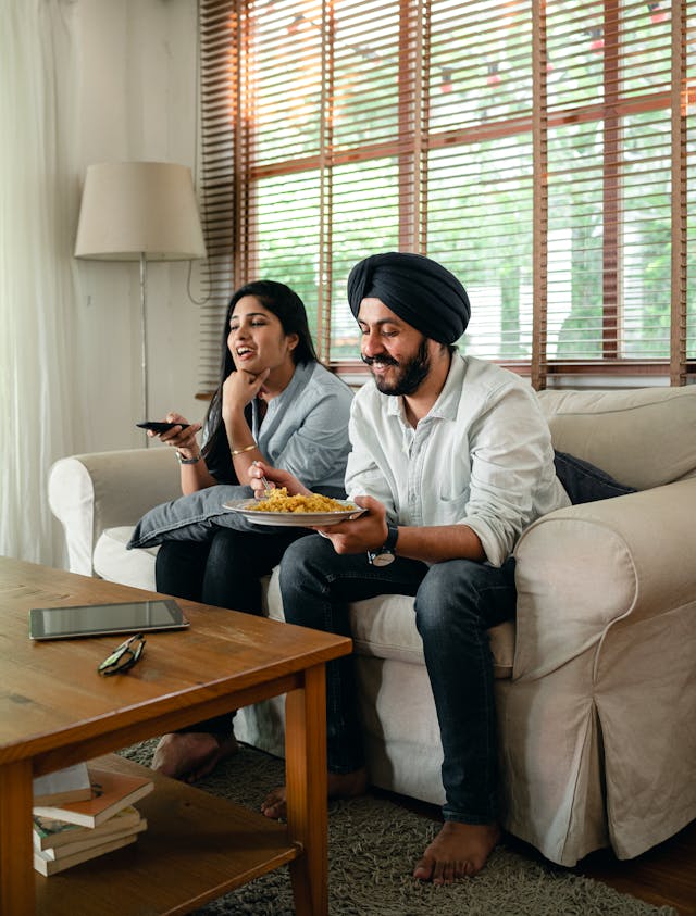 A couple enjoying their evening at home, watching TV together. They have ordered a non-veg tiffin service for dinner.